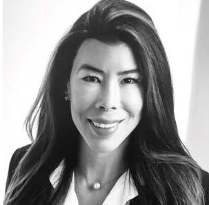 Black and white portrait of a woman with long hair, smiling, wearing a blazer and necklace.